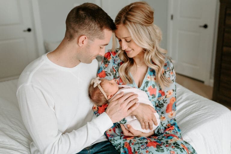 Mom and dad sitting on a bed, gazing at their newborn with warmth and love during a relaxed newborn photo session at home in Maryland.