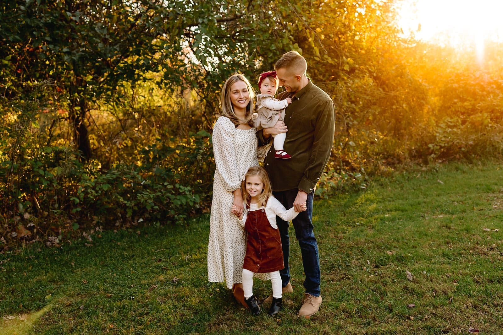 Family of four posing together in a park. Backlit by the sun.