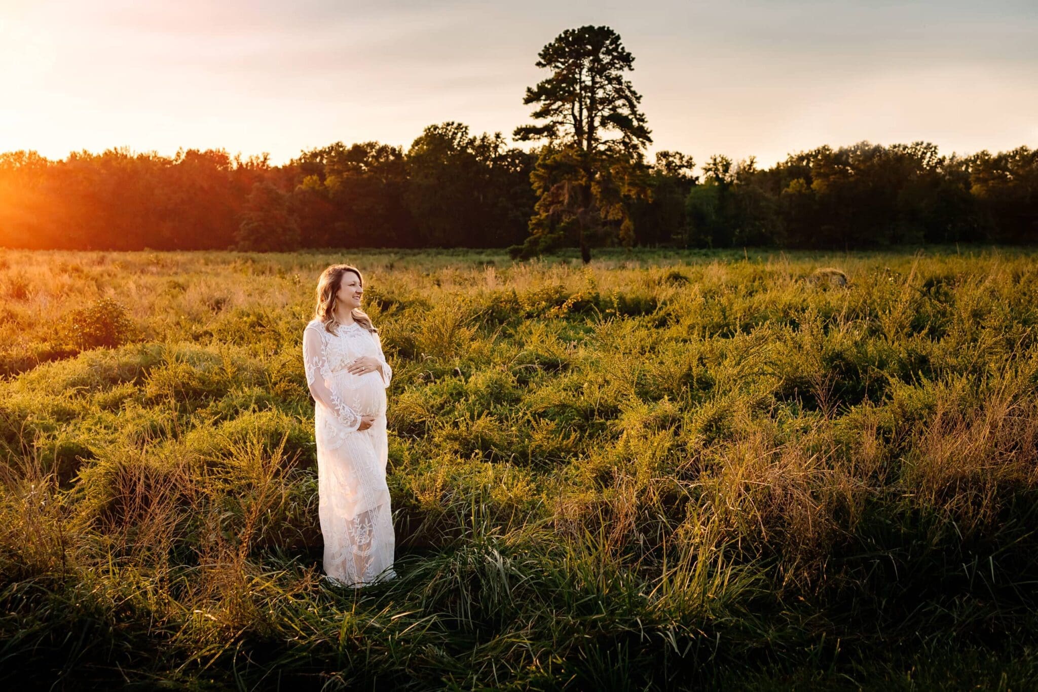 Pregnant mother posing in a grassy field at sunset.