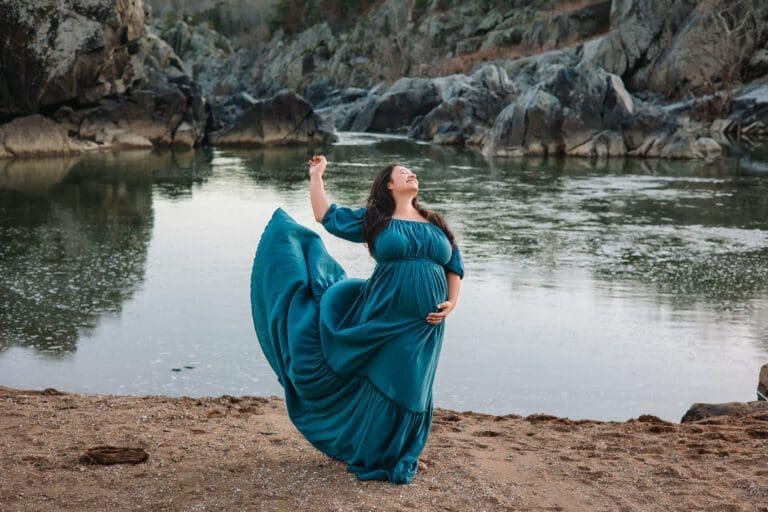 Expectant mom tossing her skirt as she poses on the water's edge at Great Falls Park.