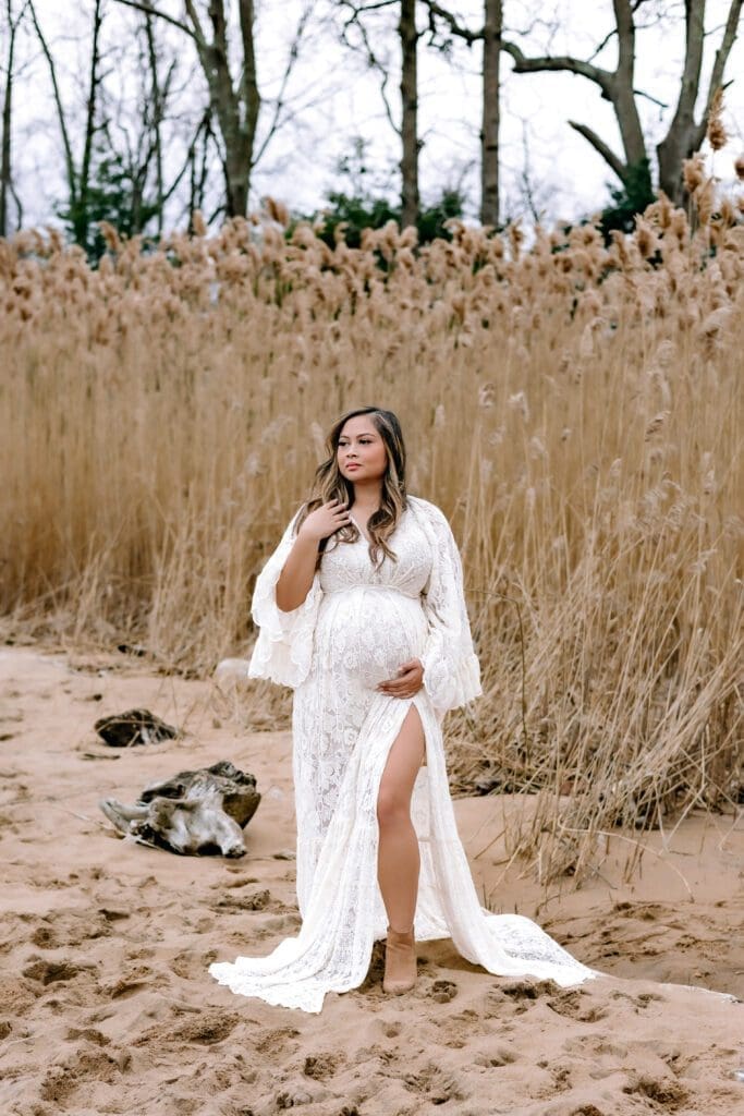 A pregnant mom in an ivory lace dress posing on the beach, cradling her belly.