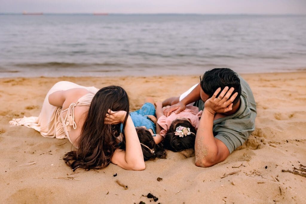 Family of 4 lay together on the sandy shore of Annapolis, MD.