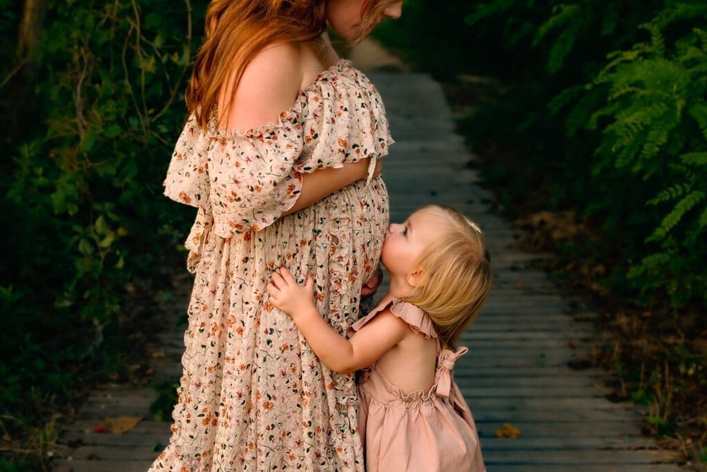 Toddler kisses mama's pregnant belly during a family photo session.