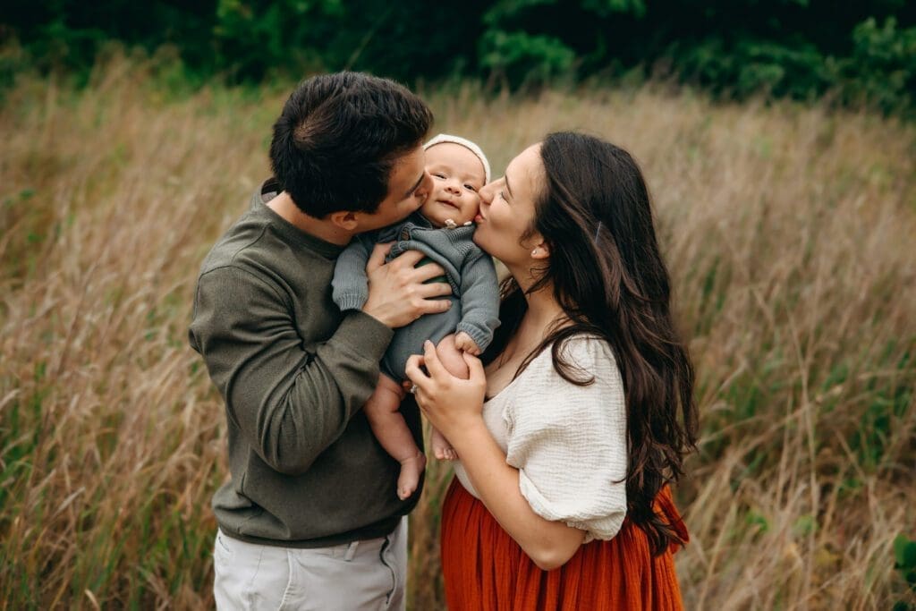 Loving parents cradle their 3-month-old baby between them, showering sweet kisses on his cheeks, capturing a tender and heartwarming family moment.