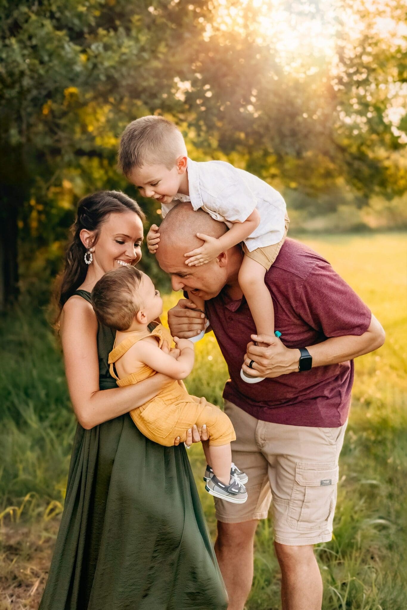 Dad carries toddler on his should and leans over to get a giggle out of the baby in mom's arms during a sunset toddler photo session.