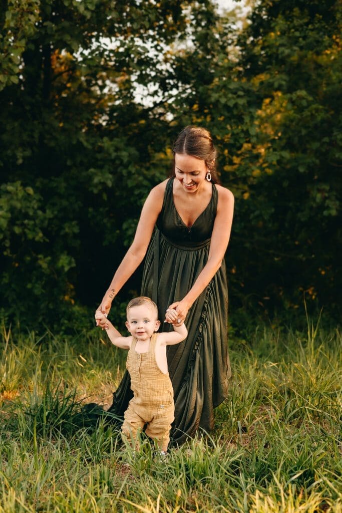 Mom holds hands to walk with her baby during a sunset photo session in Central Maryland.