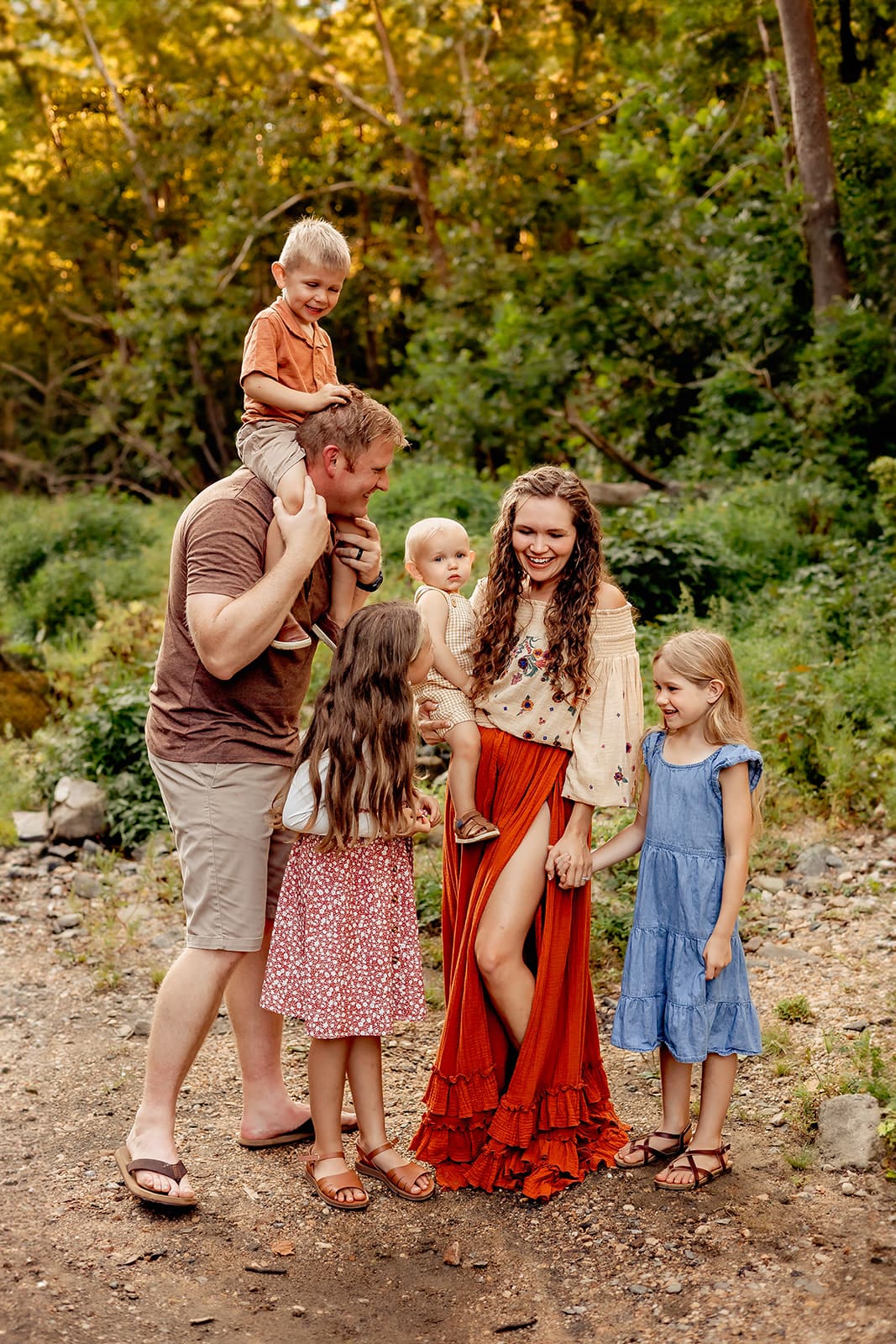 Family of five with young children posing together in a lush outdoor setting, showcasing a casual and intimate family portrait by a lifestyle photographer.