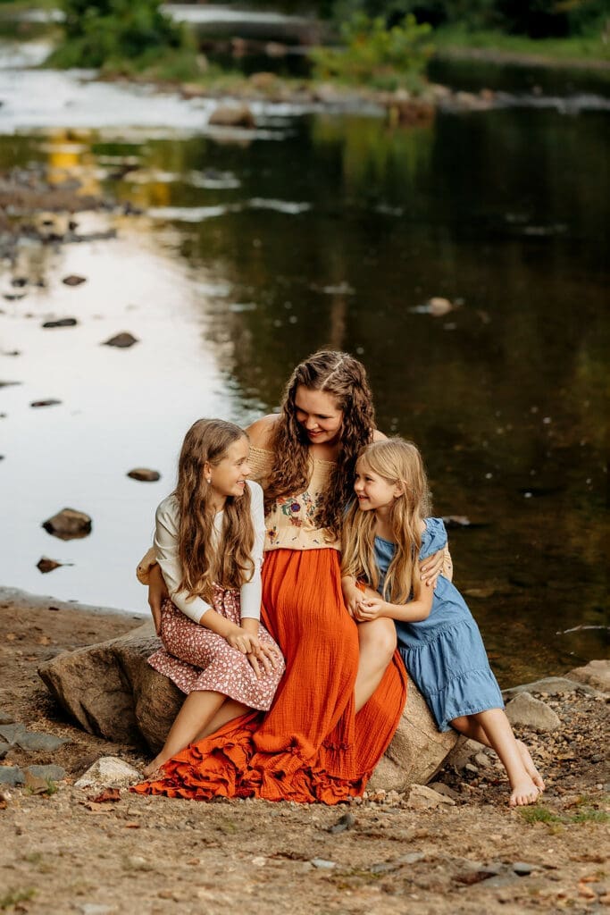 Mother sitting by the river with her young son and daughter, sharing a tender moment in a serene outdoor setting, ideal for heartfelt lifestyle photography.