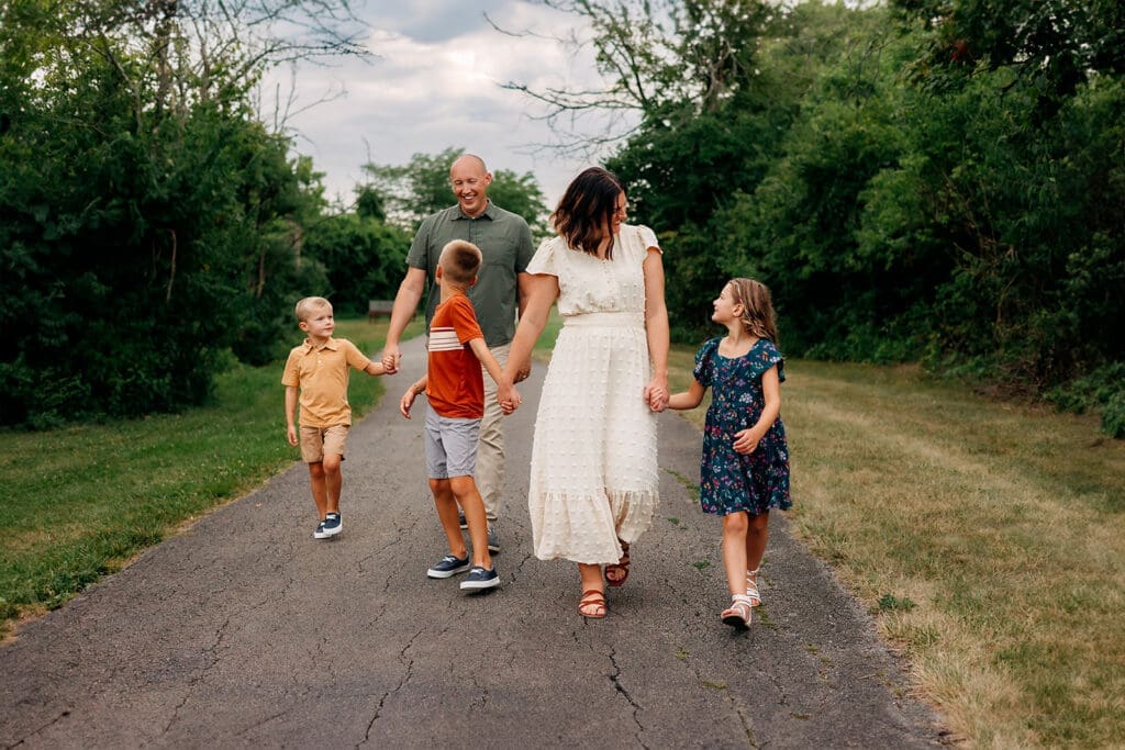 The family is walking down a path, with the parents holding hands with the children and chatting.