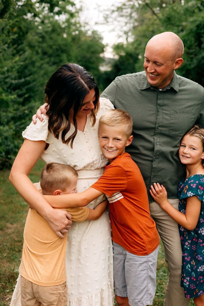 The family of five is seen together with the children hugging the mother and the father looking at them with a smile.