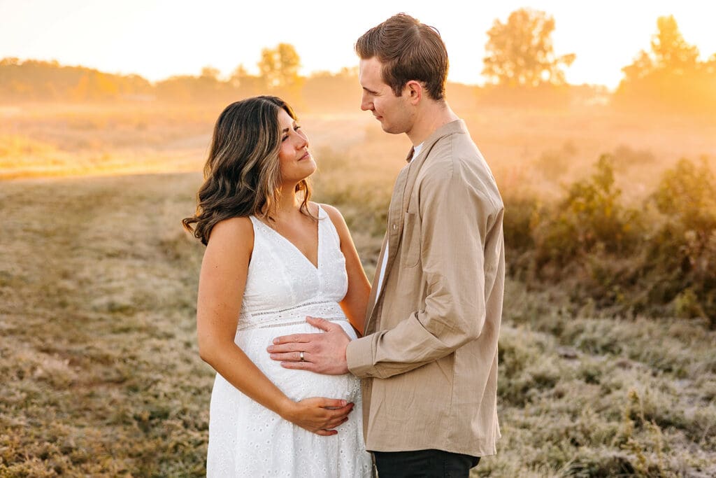 Pregnant woman and partner in a loving embrace in a foggy field, highlighting maternity photoshoot tips for a serene setting.