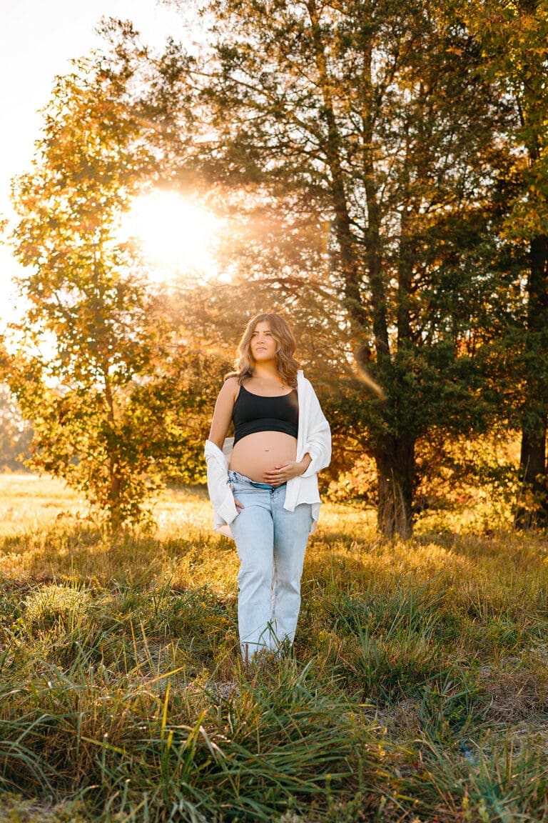 Pregnant woman standing thoughtfully in autumn sunlight amidst trees