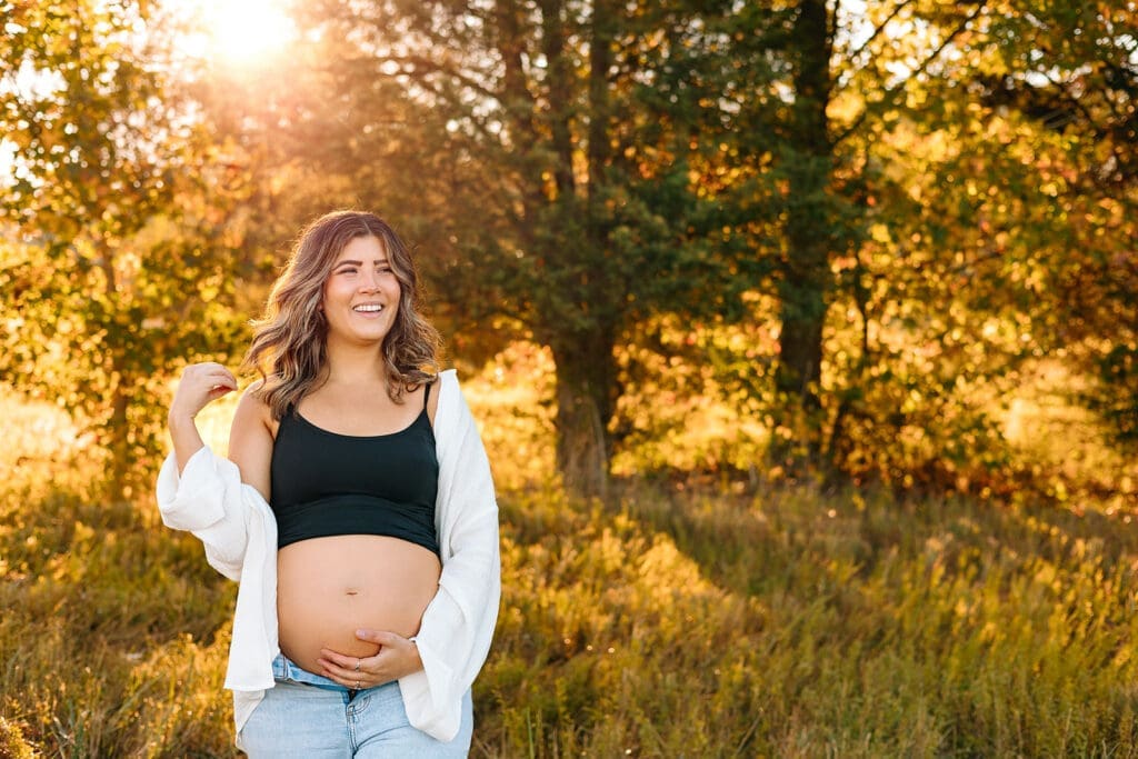 Joyful expectant mother smiling in sunlit autumn woods.