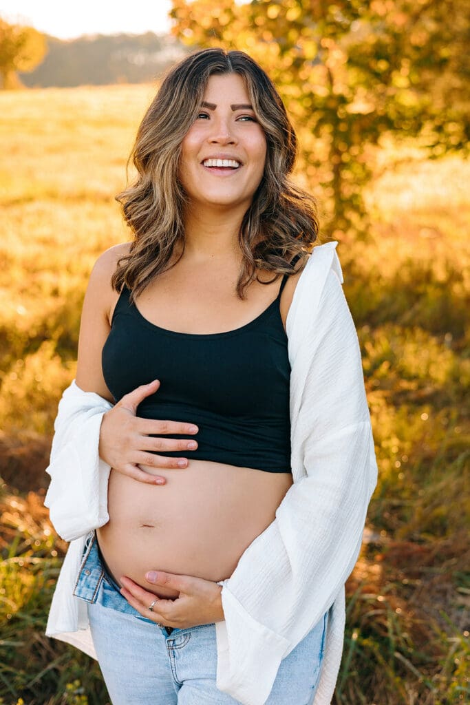 Maternity photoshoot inspiration with a smiling pregnant woman in casual attire, bathed in golden sunlight.