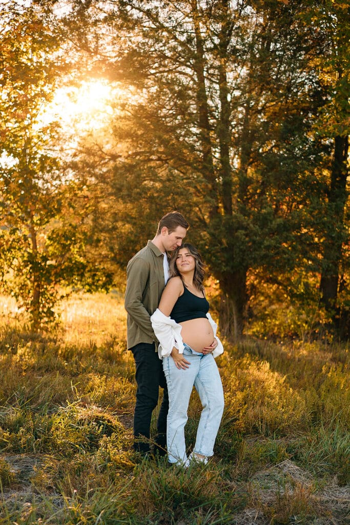 Couple bathed in sunlight during a golden hour maternity photoshoot in an open field.