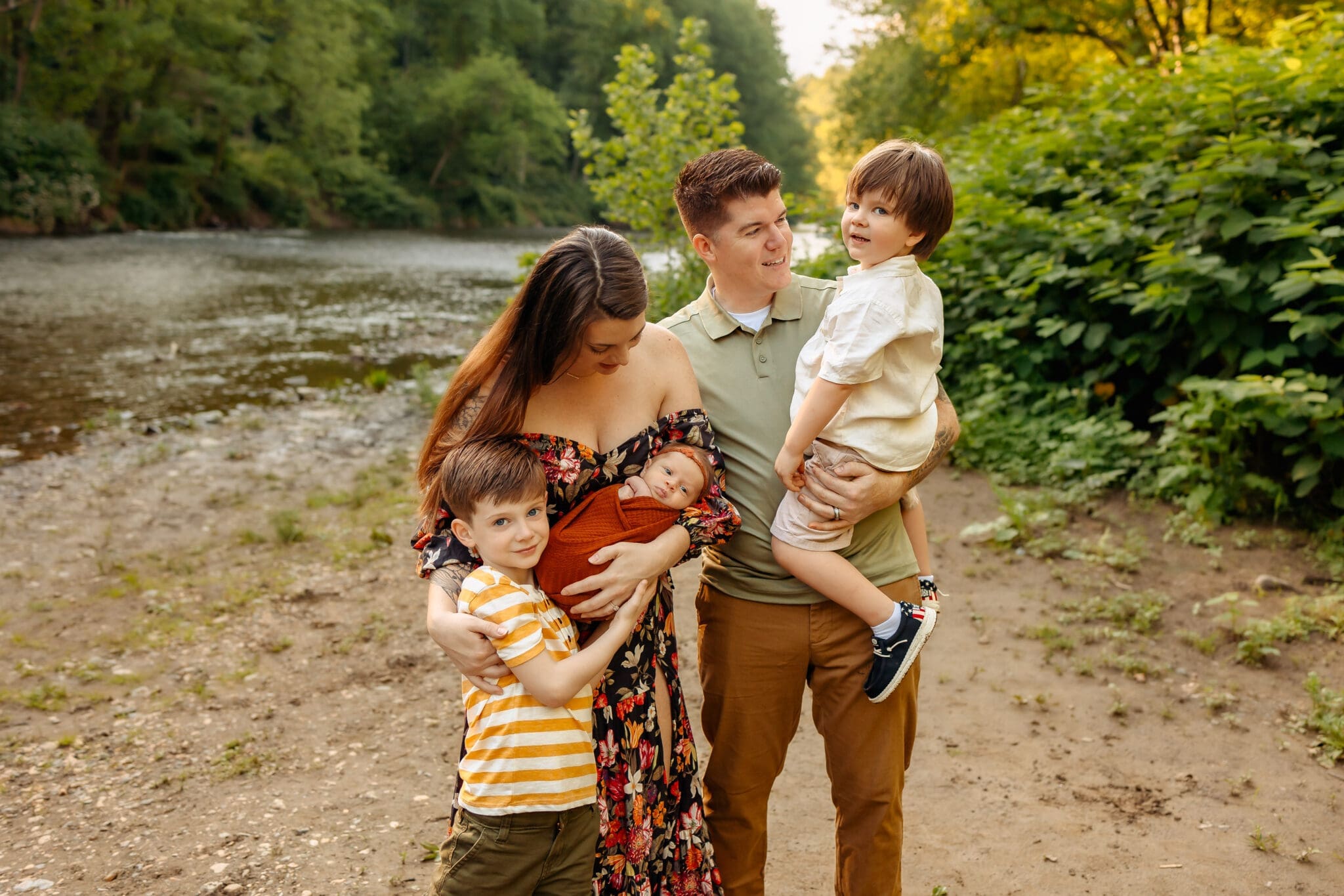 A mother embraces her older child while holding her newborn, with the father holding their other child beside them.