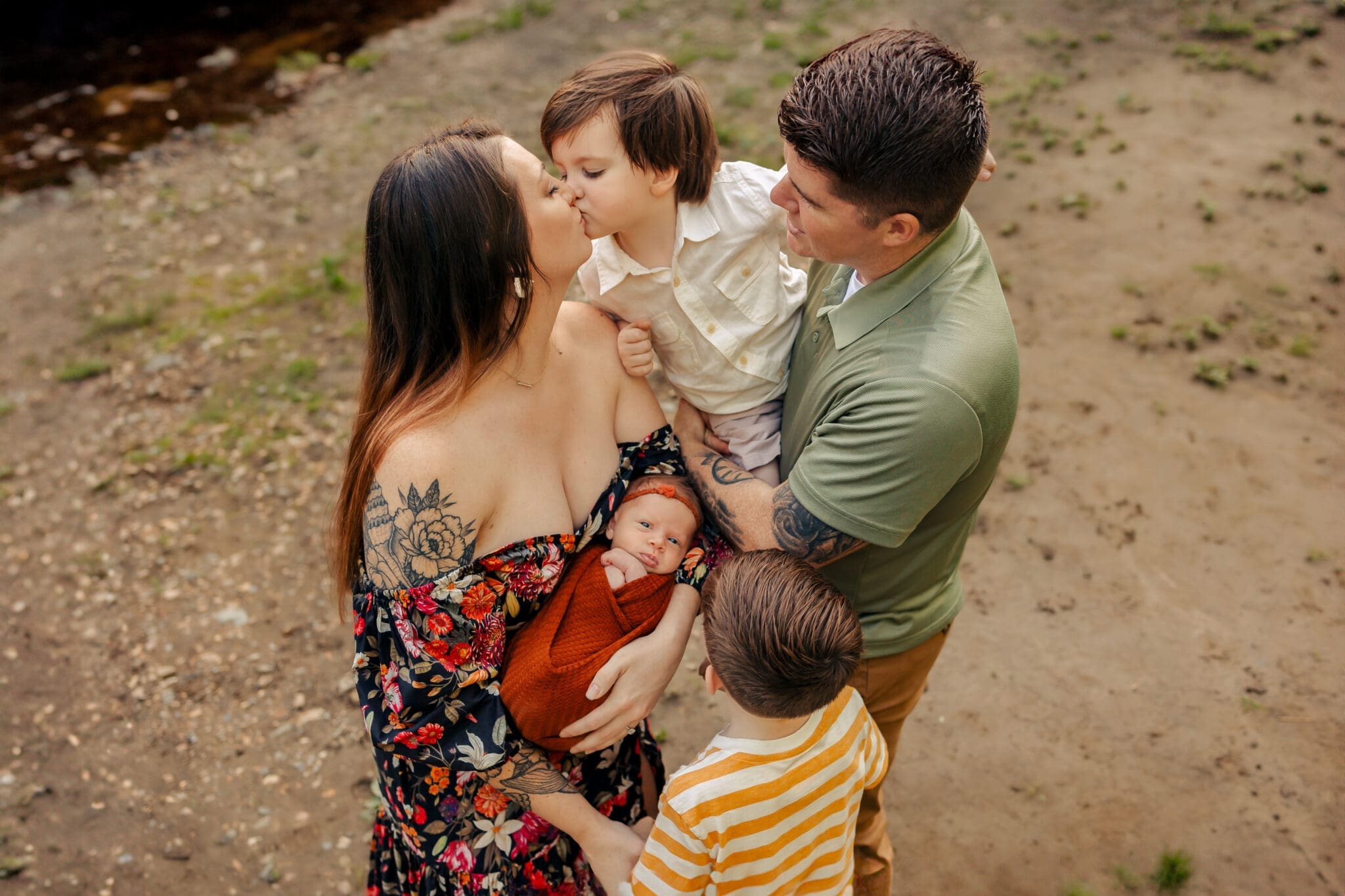 preparing-for-a-baby-in-bowie A family of five standing near a river, with the mother holding a newborn baby and the father holding another child.