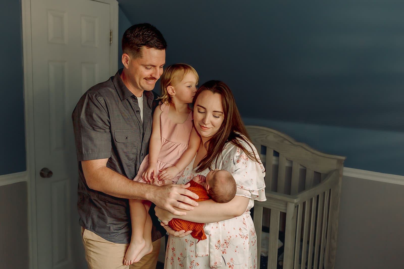 Mother and father stand together by a bright window holding their baby during an in-home newborn session in Bethesda, Maryland.