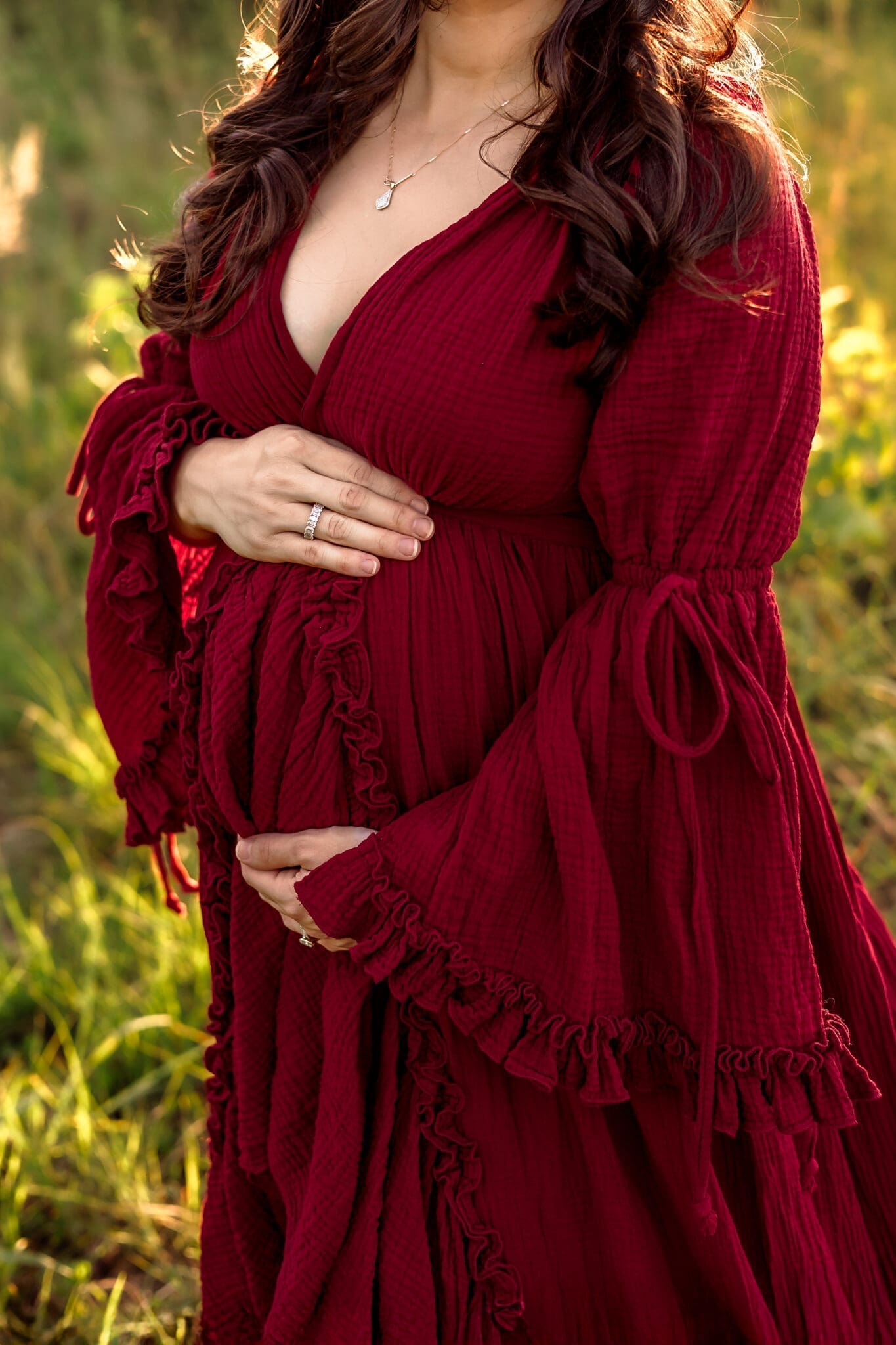 A close-up of a mother’s hands cradling her baby bump, framed by the warm glow of sunset