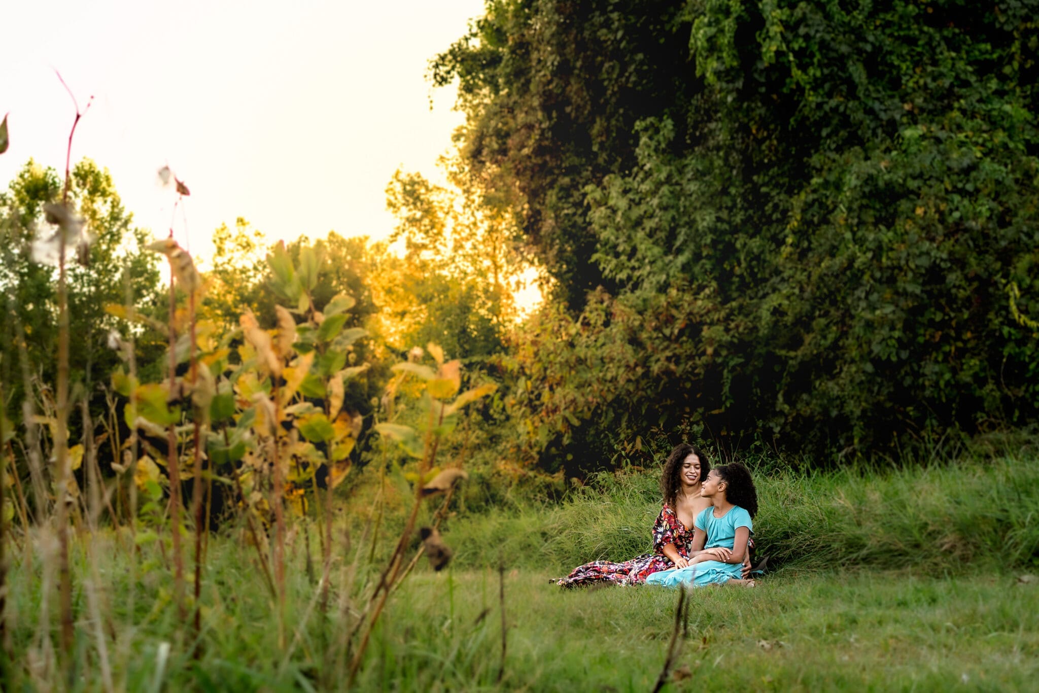 Mom and daughter cuddling and laughing together in a field at golden hour for their Mothers Day family photos in Maryland.