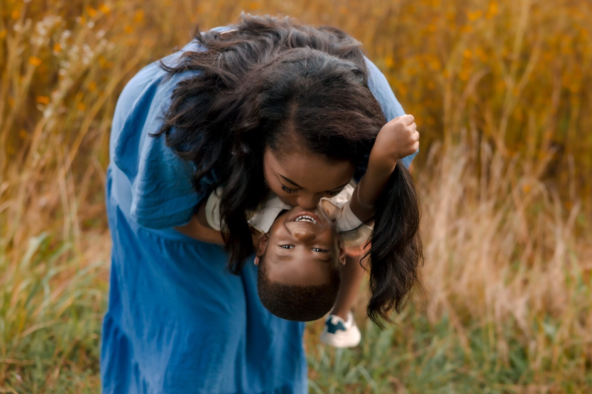 A mother bends down to kiss her young child’s forehead during a lifestyle family photography session in Maryland, with greenery in the background.