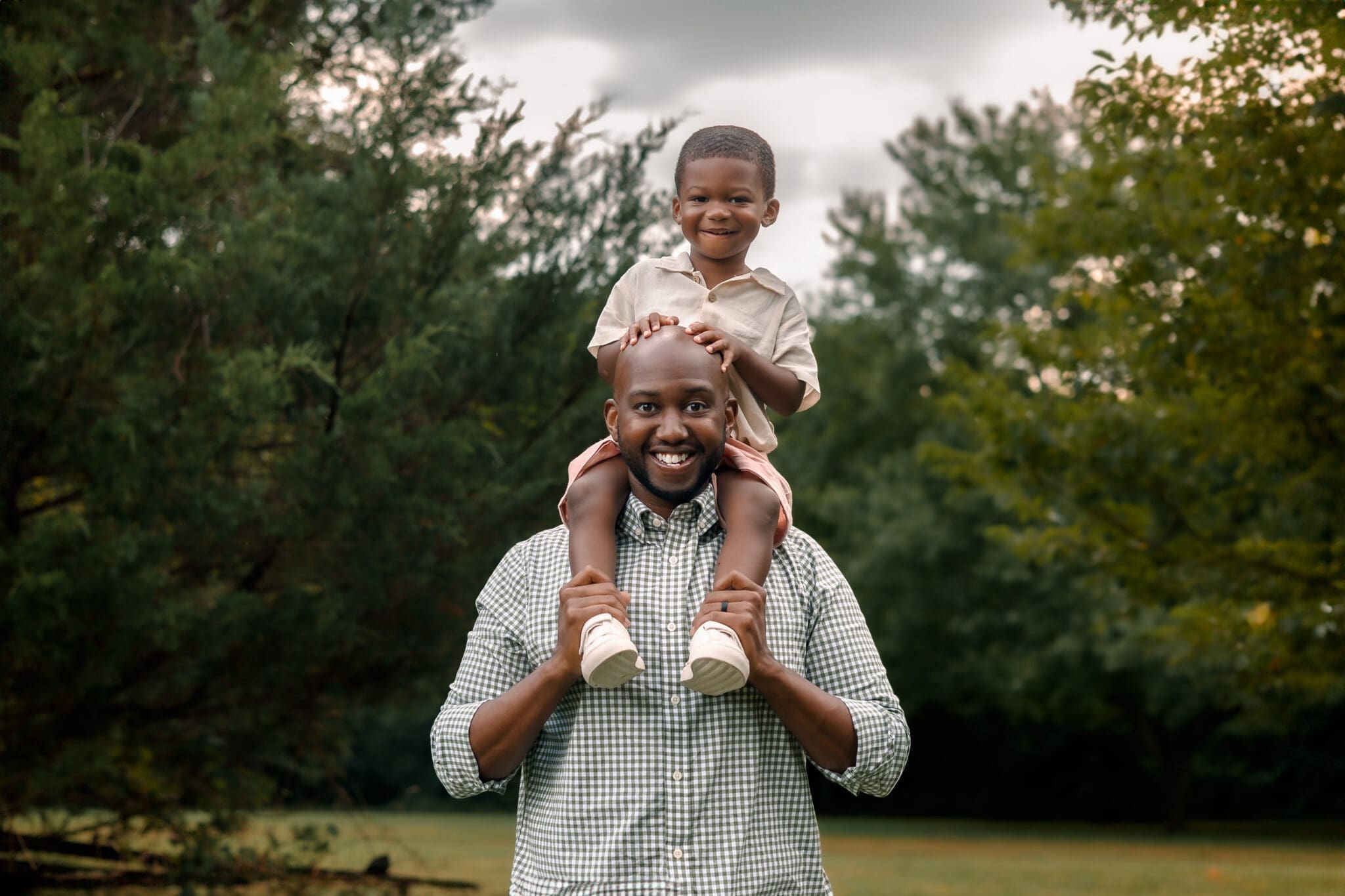 Father holding son on shoulders and smiling in open field