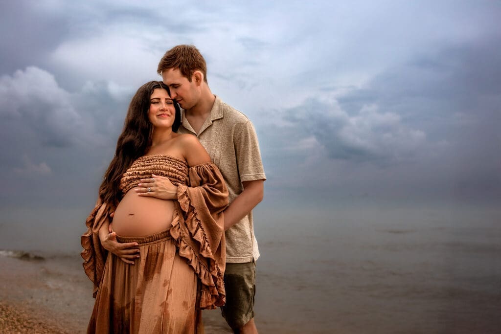 Couple holding hands during an Annapolis beach maternity photography session, with gentle waves rolling in.