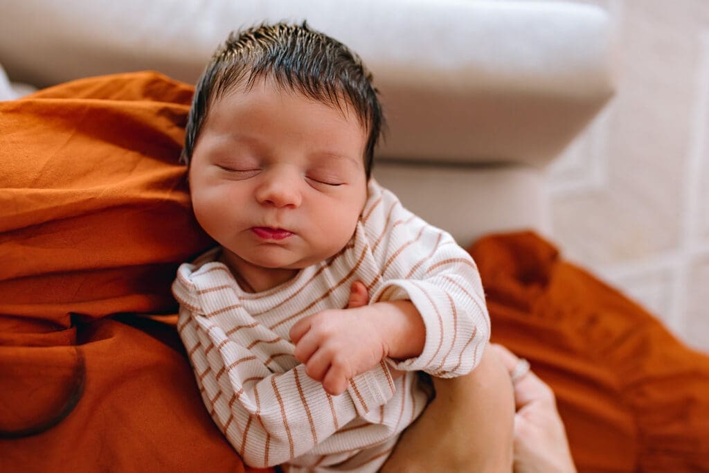 Newborn swaddled in a rust-colored blanket sleeping peacefully during an in-home newborn session in Bethesda, Maryland.
