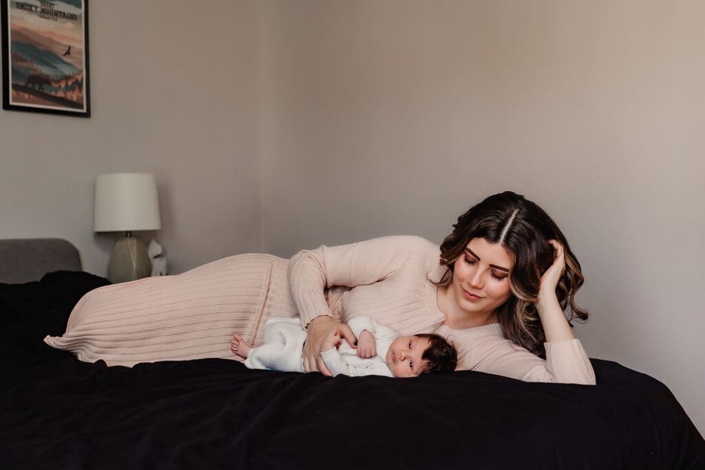 Mom reclines on her bed holding her swaddled baby during a lifestyle newborn photography session in Bethesda, Maryland.