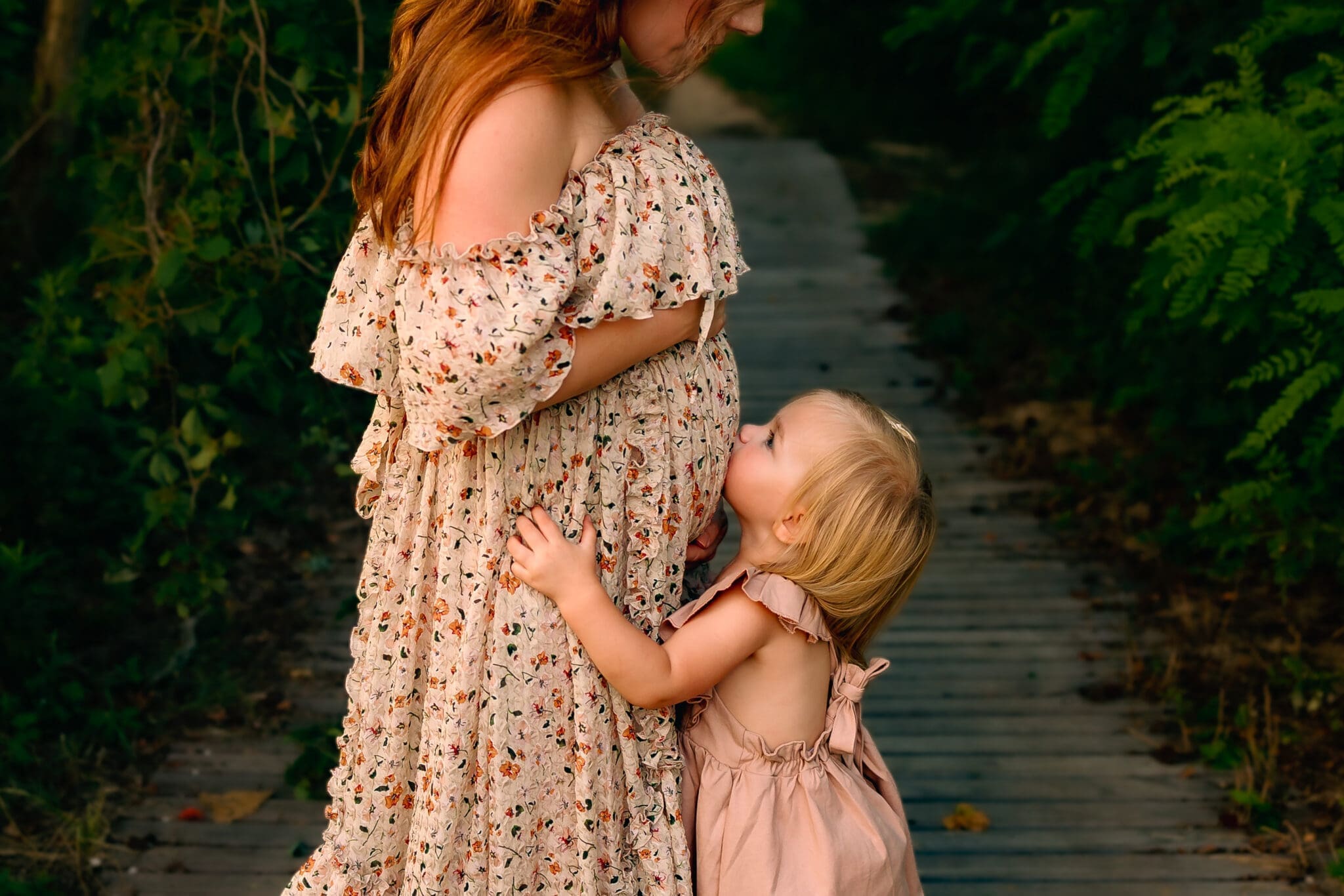 Mother and young daughter share a hug in a field during a Maryland maternity photography session.