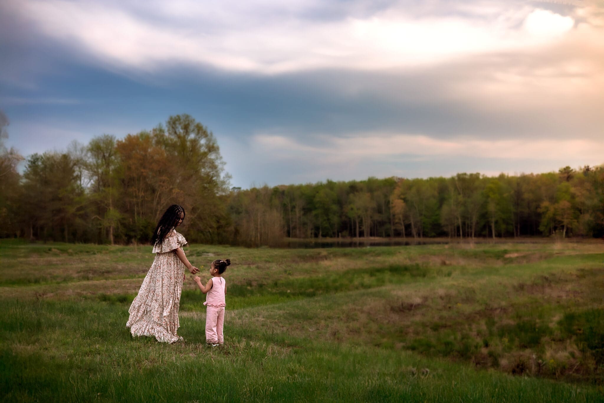 A mom stands in an open field taking a flower from the hand of her young daughter