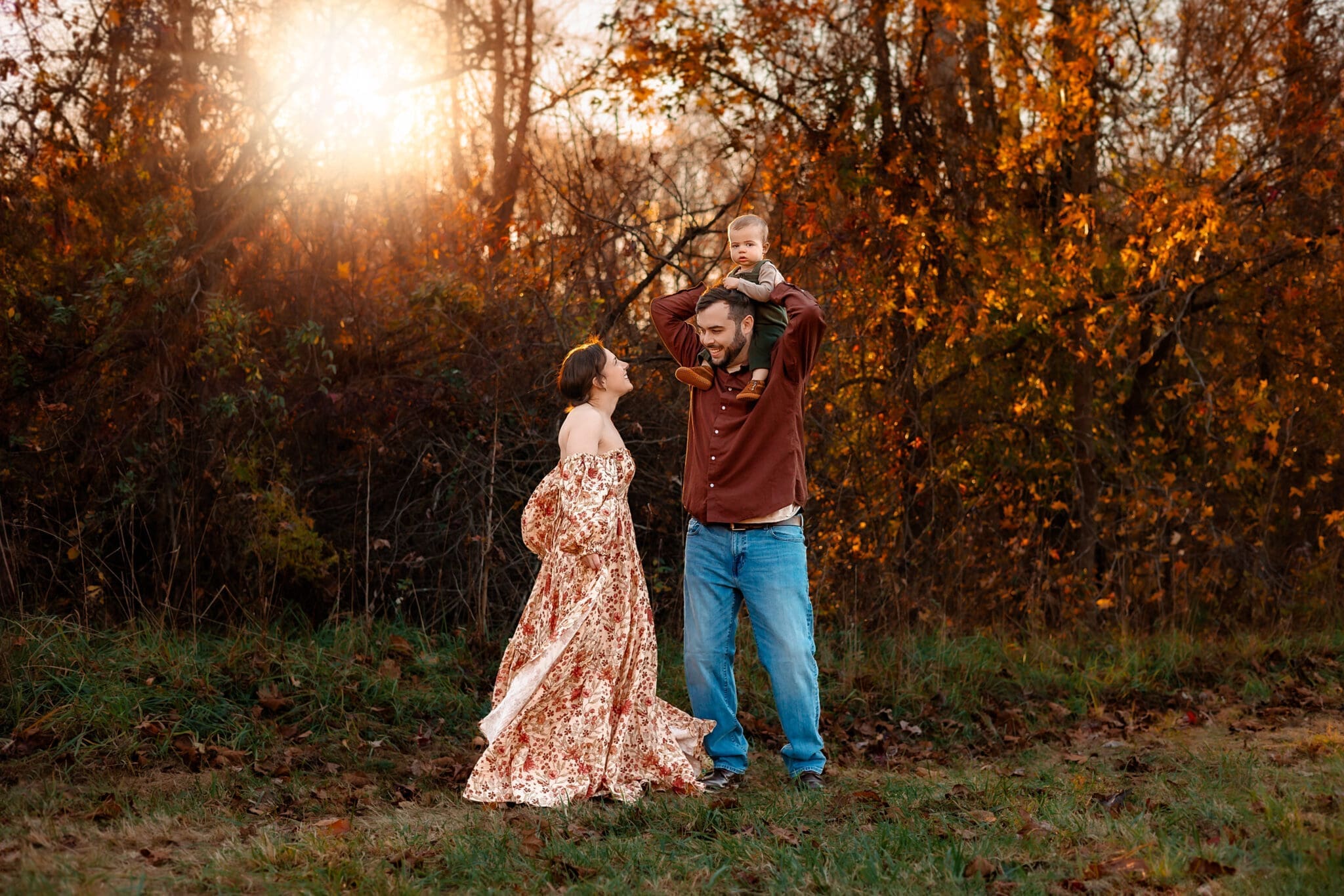 A family stands together in a sunlit autumn field during a lifestyle family photography session in Maryland, with golden leaves in the background.