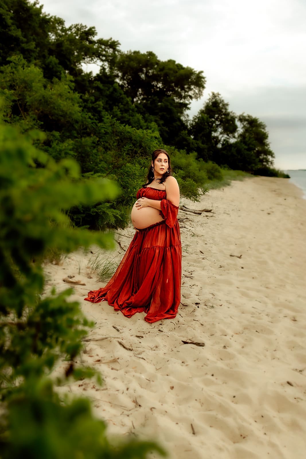 An expectant mother cradles her bump as she gazes across the sand towards the bay.