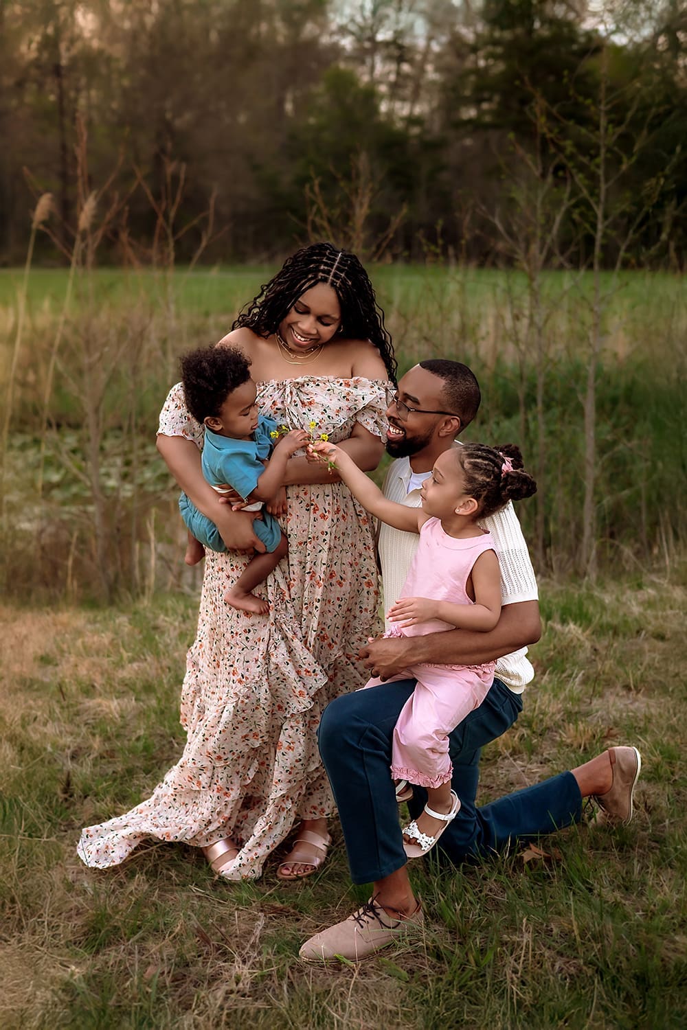 A photo of a smiling family of four sharing a playful moment together in a grassy field, with parents holding their young children on a warm evening. Taken by Erin Link, Maryland Family Photographer in Bowie.