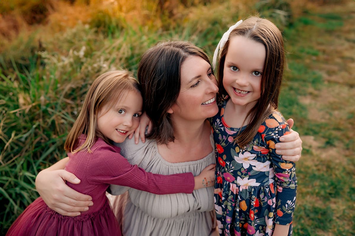 Erin Link, a Maryland family photographer, shares a joyful moment with her two daughters during an outdoor session in Bowie.