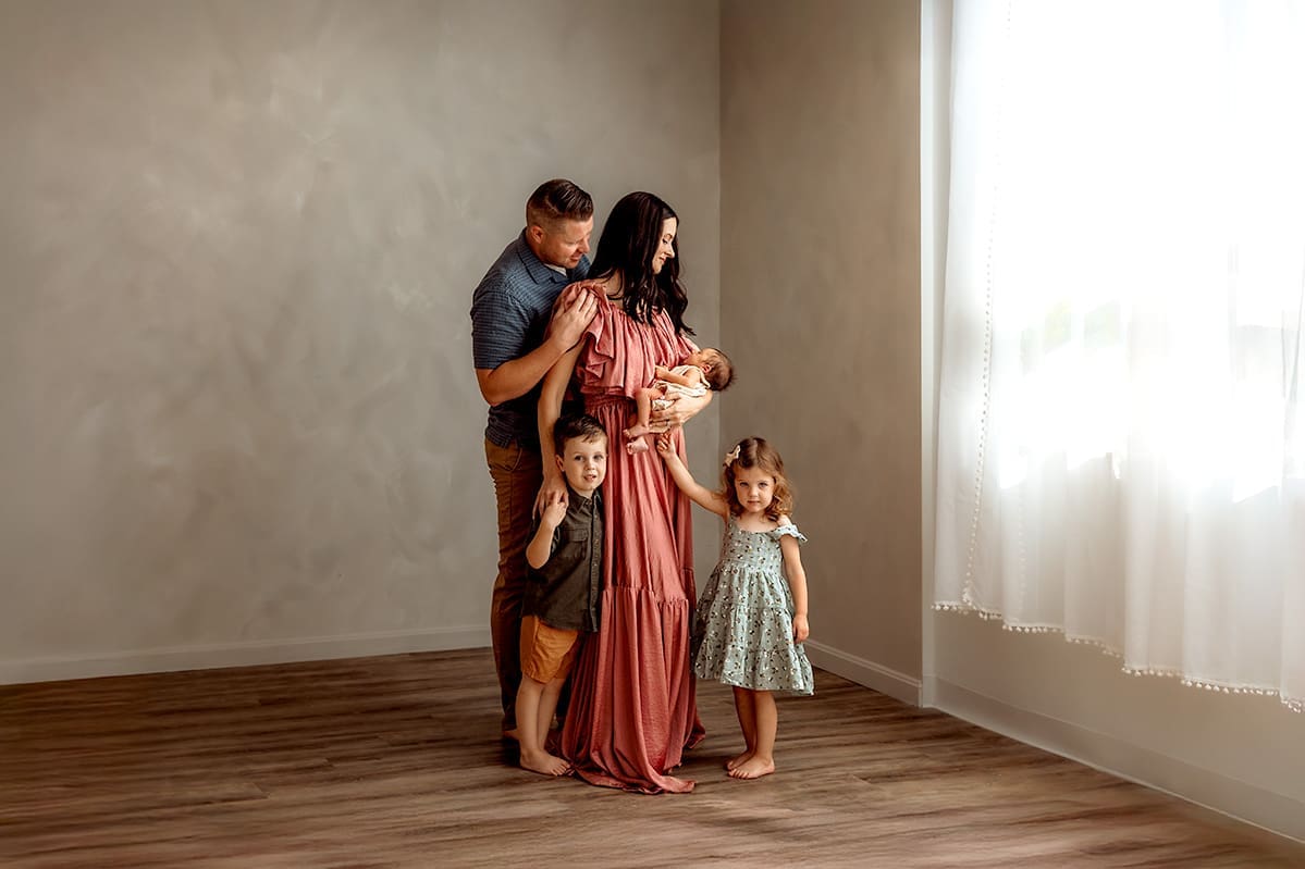 Family of five indoor portrait in Maryland studio - parents with newborn baby and two young children in natural window light