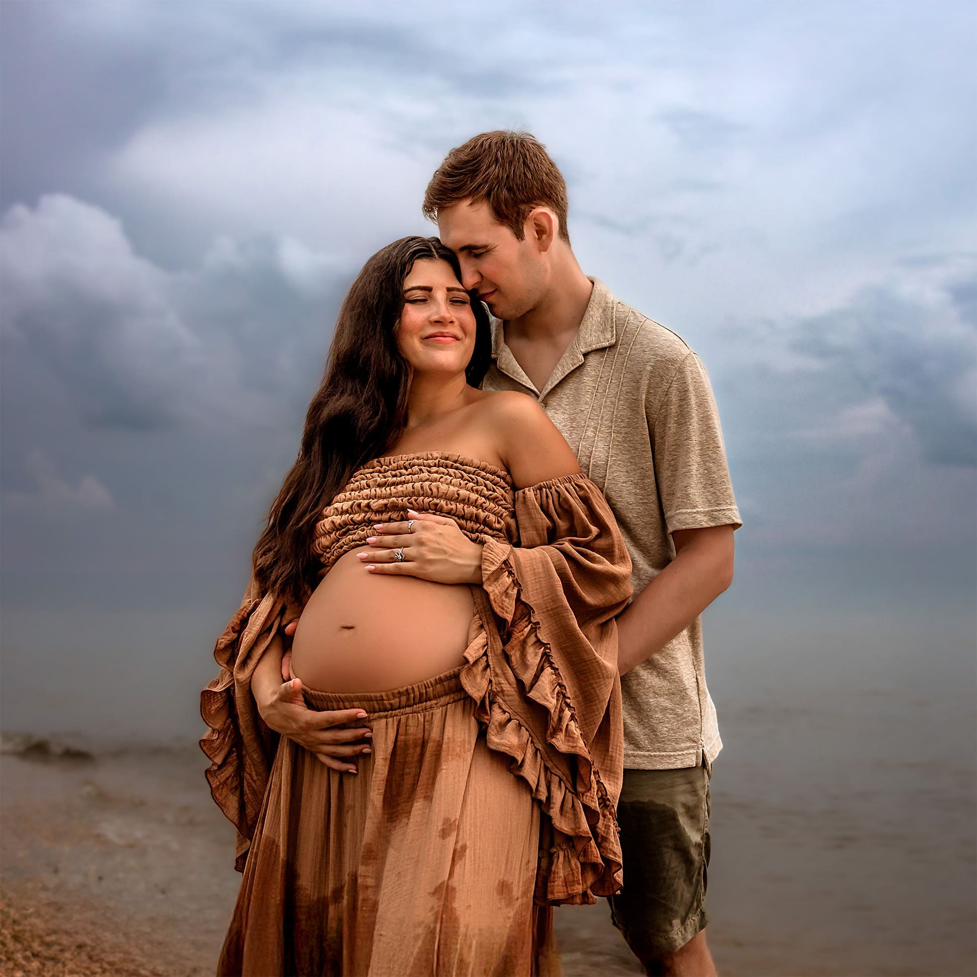 Couple holding hands during an Annapolis beach maternity photography session, with gentle waves rolling in.