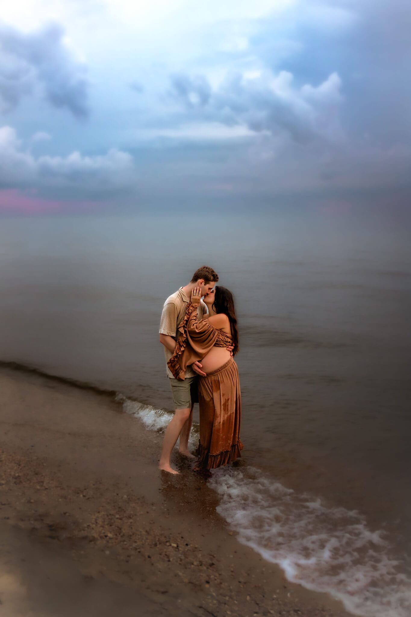 Expecting couple sharing a tender kiss at the water's edge during a Maryland beach maternity session