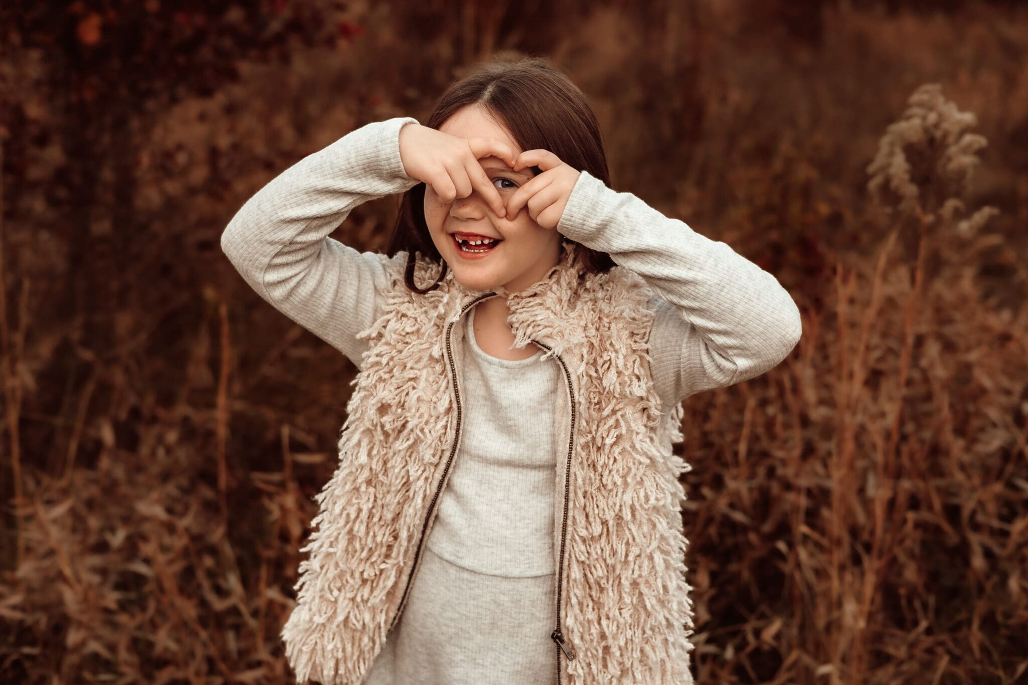 Spirited child making a heart with her hands during a relaxed lifestyle family photoshoot outdoors.