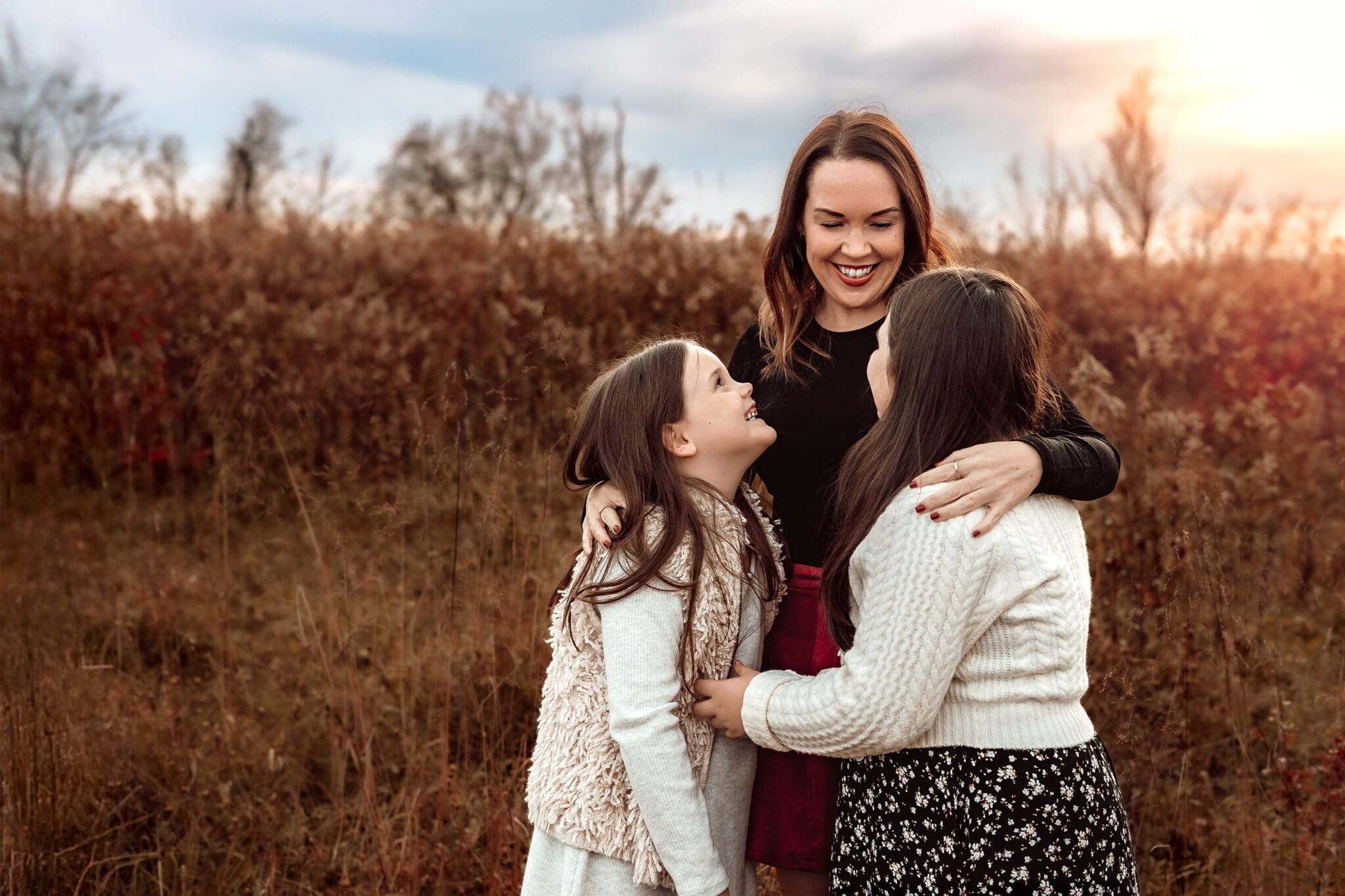 Mother smiling at her daughters while taking happy family photos with spirited kids during an outdoor family photography session in Bowie, Maryland.