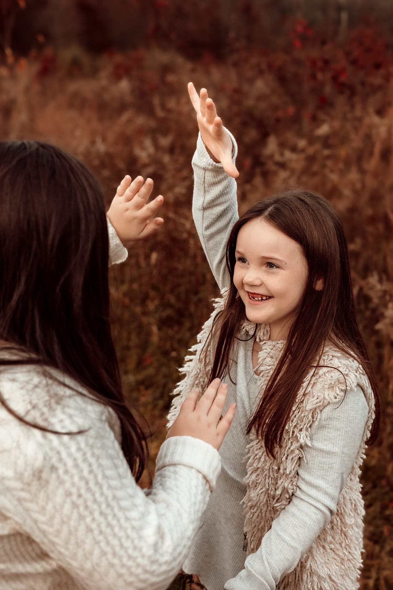 Playful moment during a photoshoot with kids as a young girl smiles and raises her hands outdoors in Bowie, Maryland.
