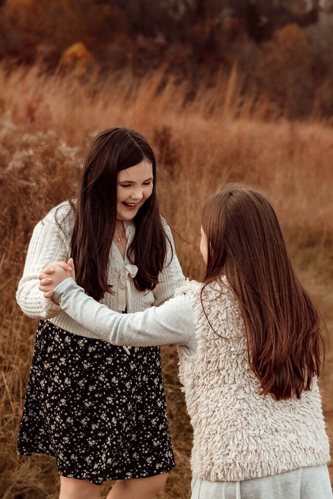 Two sisters laughing and holding hands during an outdoor lifestyle photoshoot with kids in Bowie, Maryland.