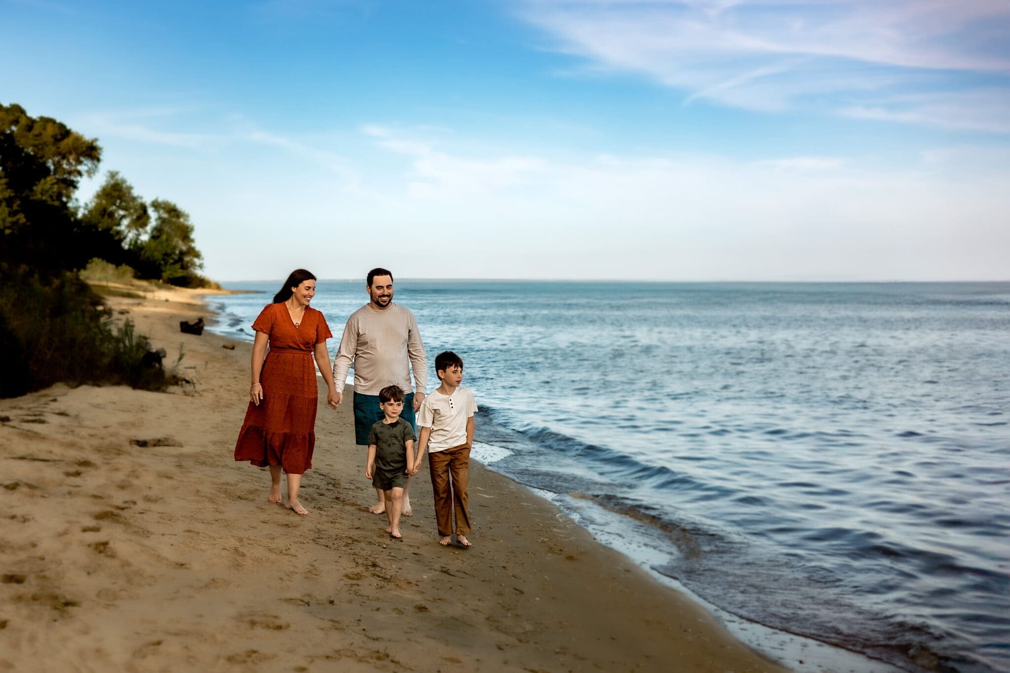 Family of four walking along a sandy beach with water in the background