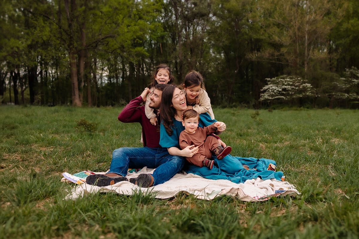 Family of five sitting together in a field, wearing burgundy and teal